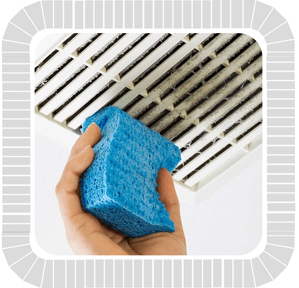 A person cleaning an air conditioner with a blue sponge for ventilation maintenance.