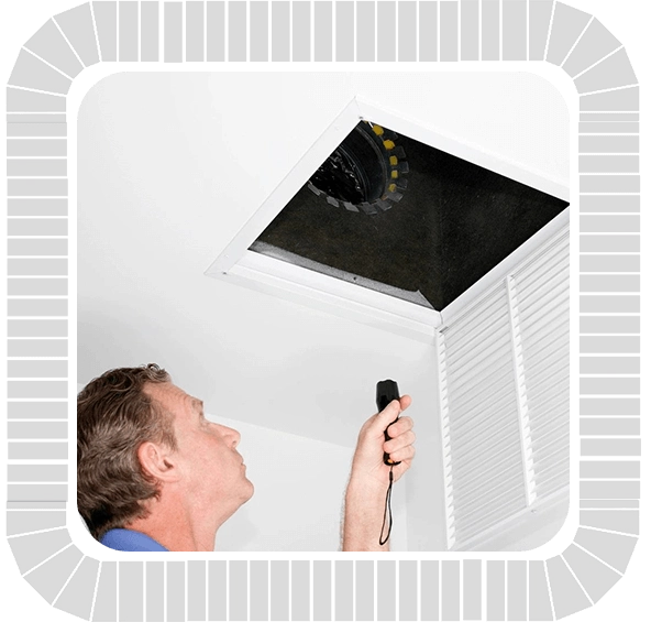 A man performing ventilation cleaning by inspecting an air conditioner in the ceiling.